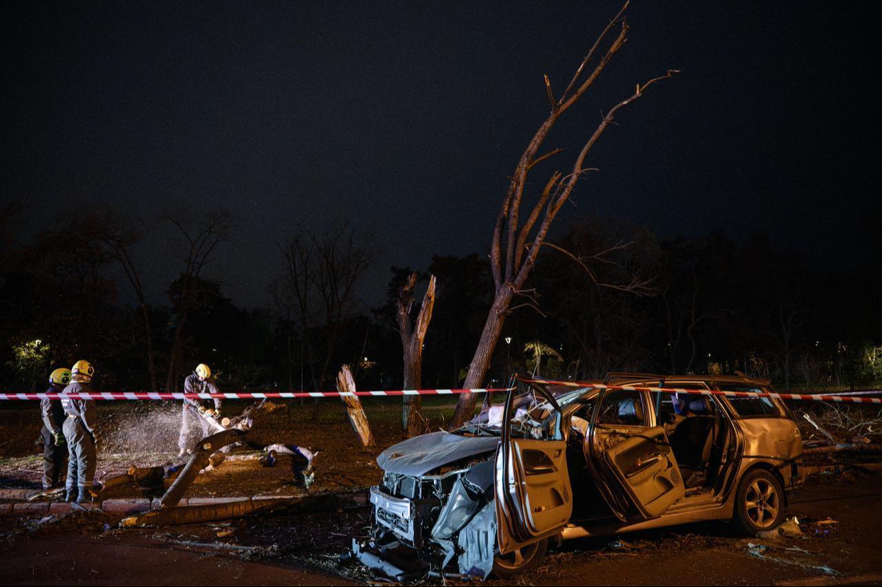 Ukrainian rescuers clear fallen trees near a destroyed car on a road in Kyiv on October 27, 2026, following a Russian missile strike. (AFP Photo)