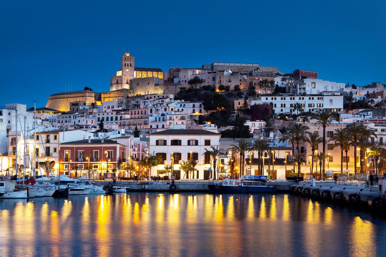 Illuminated historic buildings overlook the harbor in Ibiza, Spain, at dusk. (Adobe Stock Photo)
