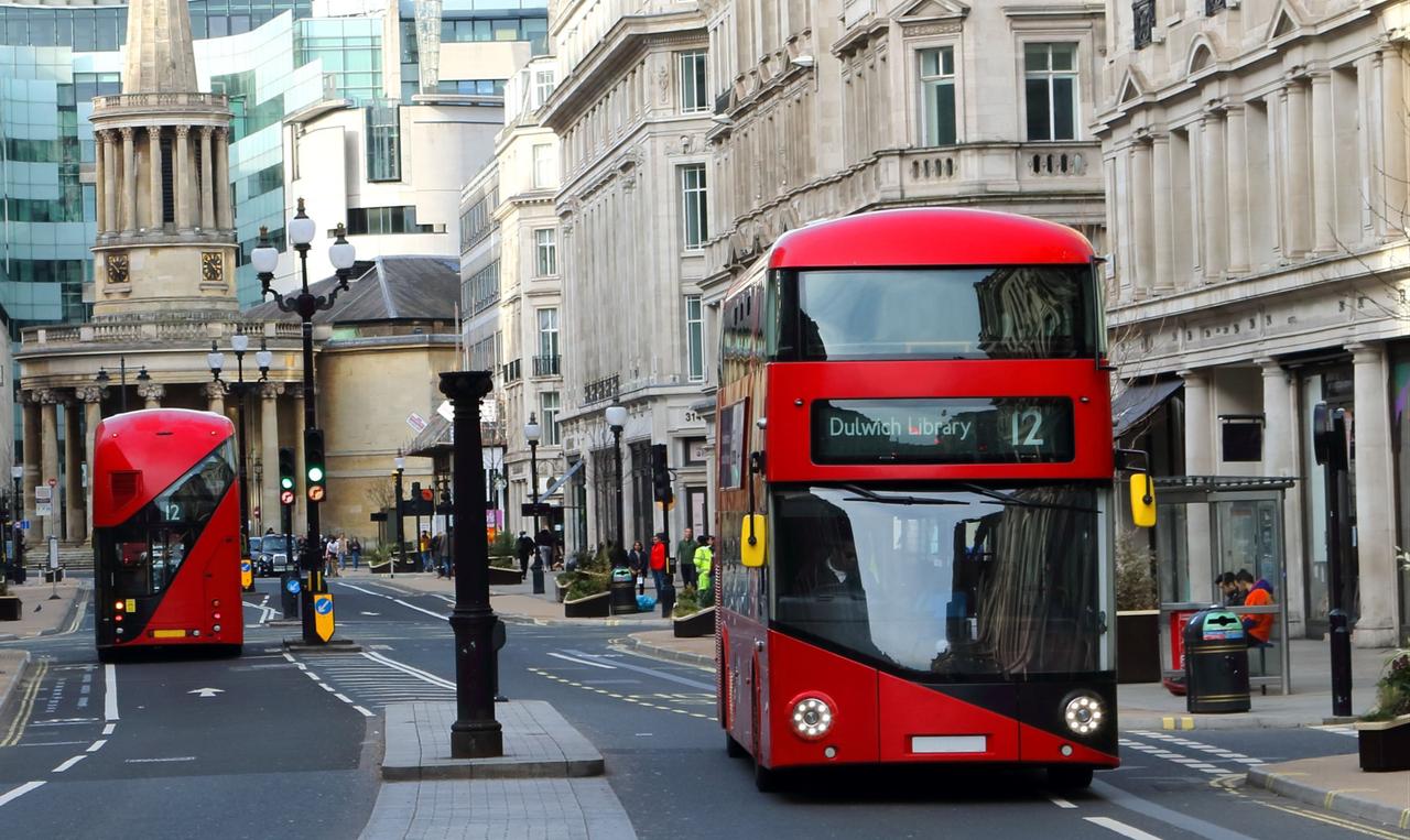 Red double-decker buses travel along a street lined with historic buildings in central London, England, U.K. (Adobe Stock Photo)
