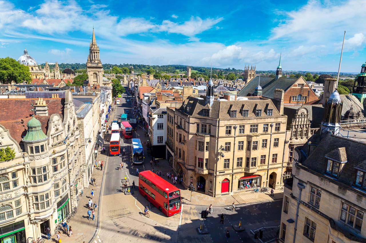 An aerial view shows historic buildings, streets and red double-decker buses in Oxford, England, U.K. (Adobe Stock Photo)