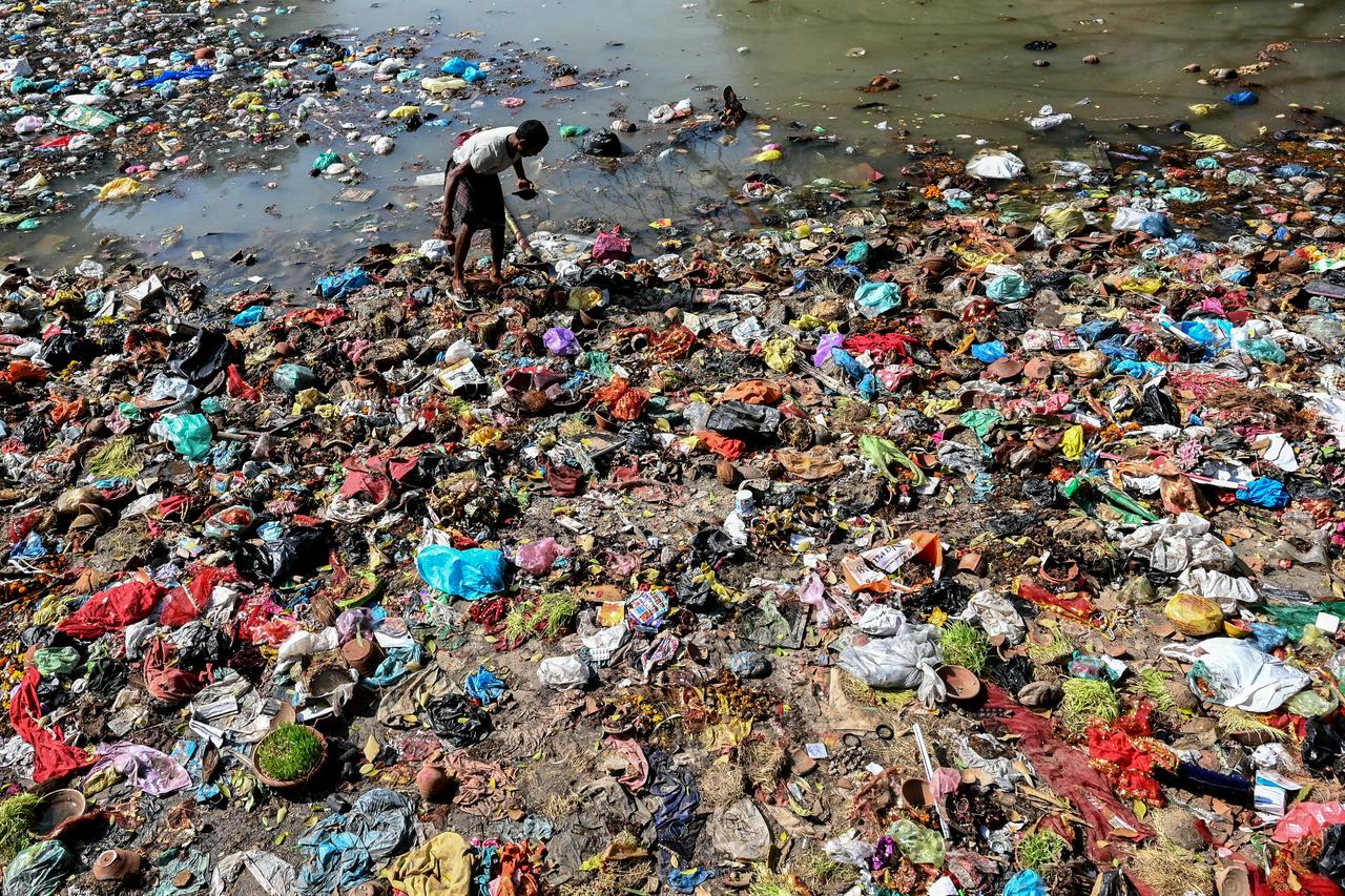 A ragpicker searches for recyclable materials and money thrown by people, as part of ritual offerings, among garbage along a canal in Amritsar on Oct. 25, 2026. (AFP Photo)