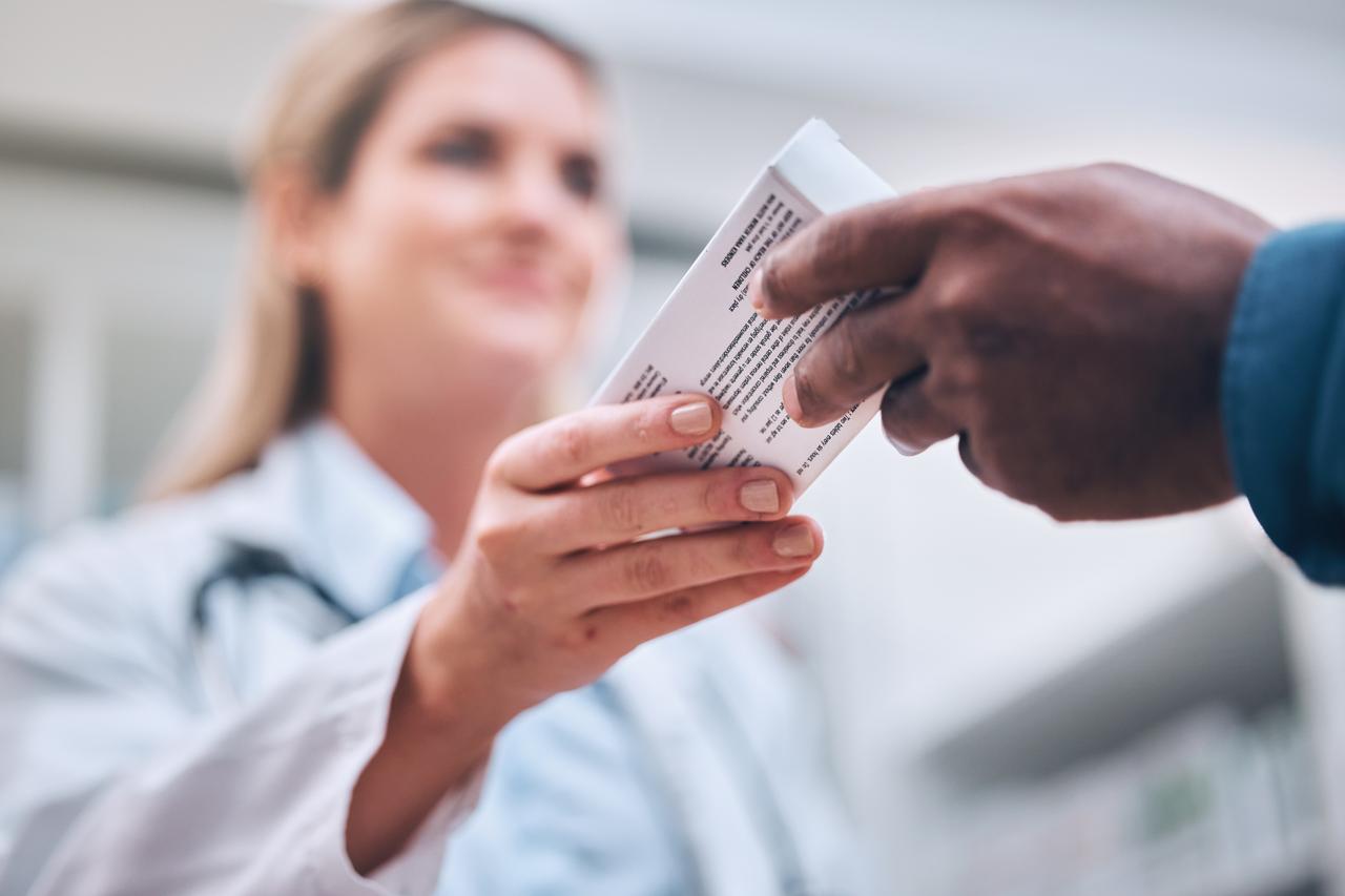 A healthcare professional hands a box of medication to a patient in a medical setting. (Adobe Stock Photo)