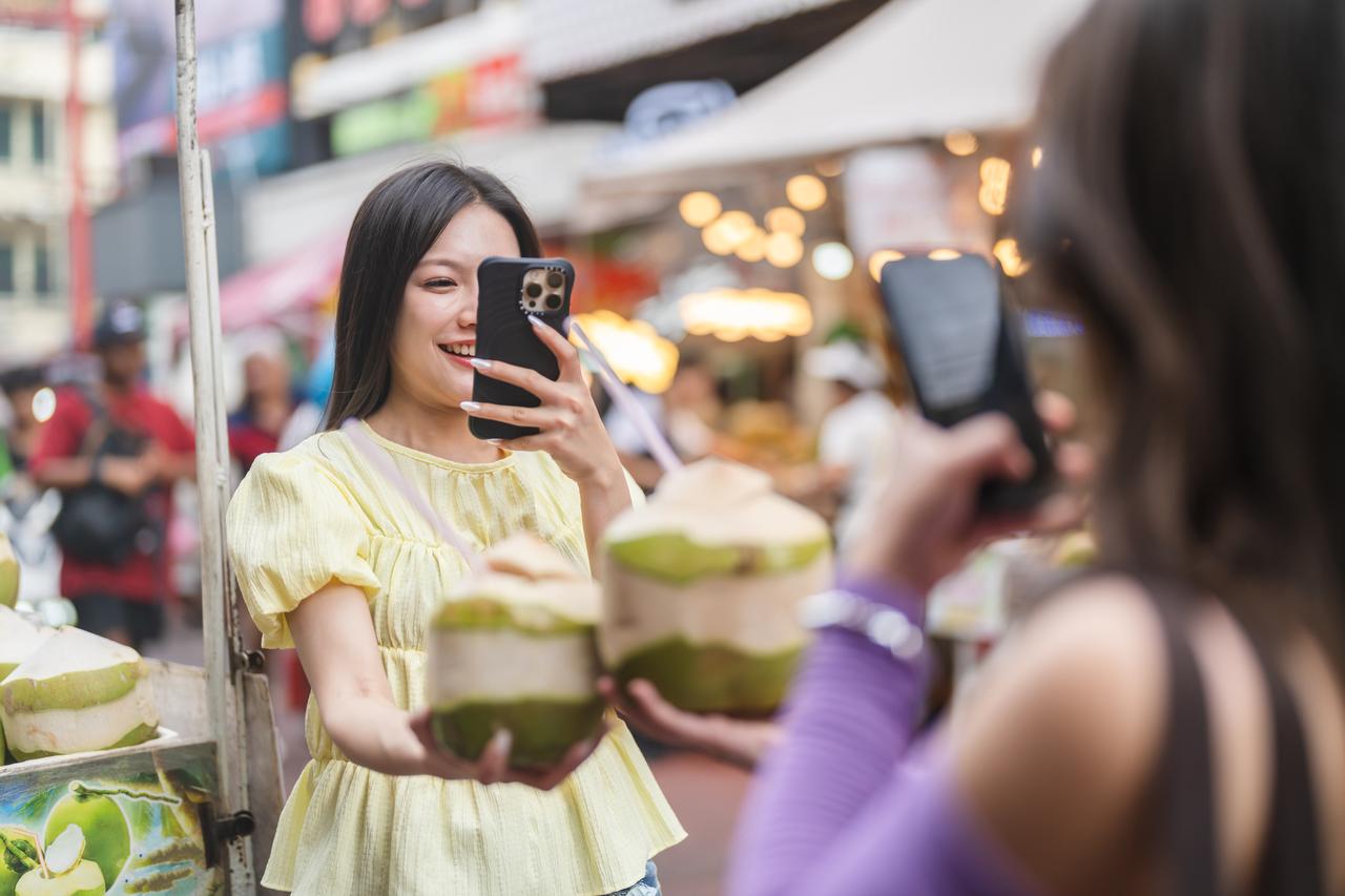 Two tourist taking photo of fresh coconuts with their smartphones at local street food market. (Adobe Stock photo)