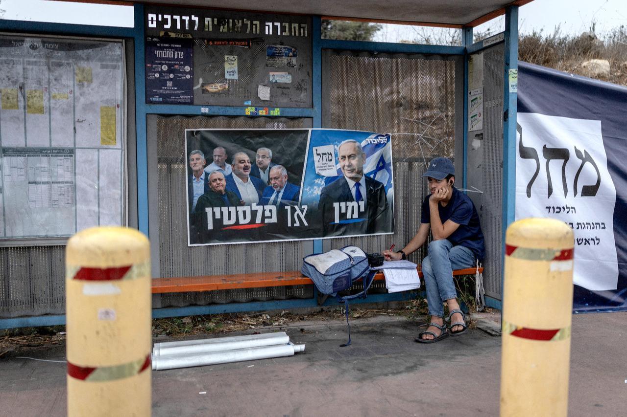 A young Israeli settler sits doing schoolwork at a bus stop adorned with election material for Prime Minister Benjamin Netanyahu's Likud party, outside the Palestinian village of Haris in the Israeli-occupied West Bank on October 26, 2026. (AFP Photo)