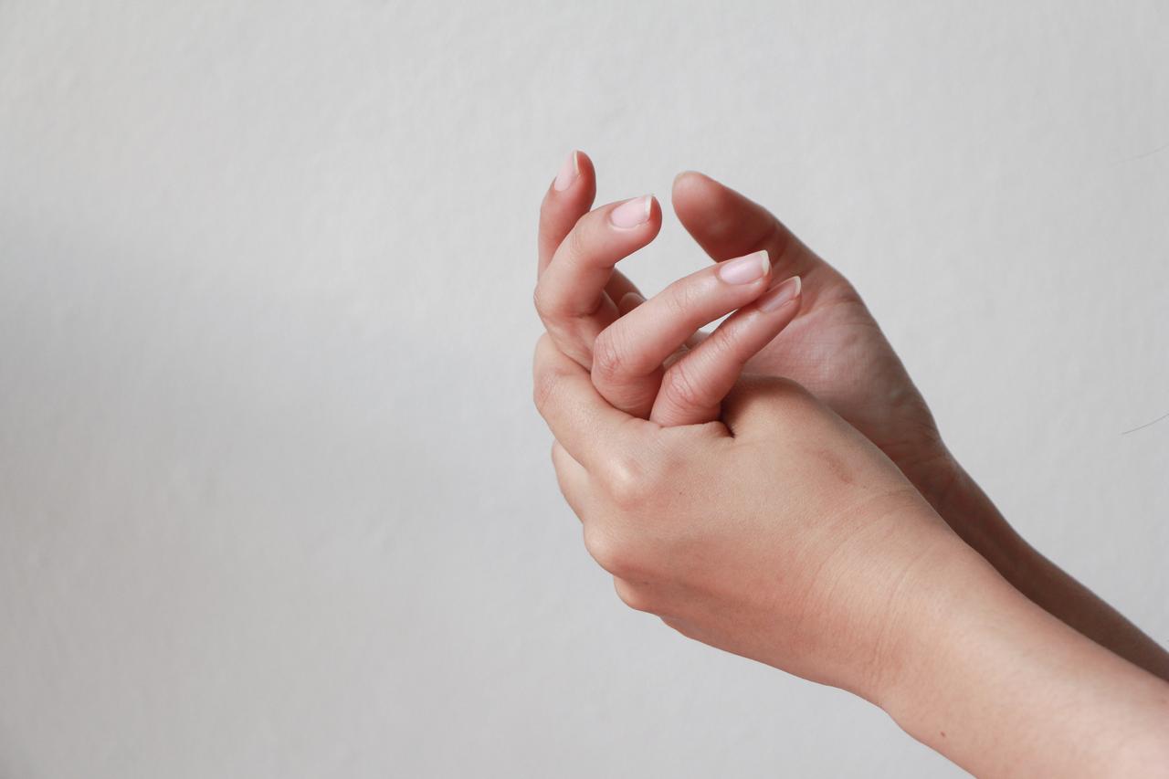 A close-up of a person clasping their hands against a neutral background. (Adobe Stock Photo)