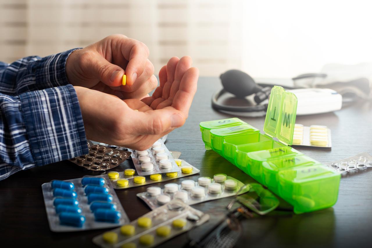 A person organizes medication using a weekly pill dispenser at home. (Adobe Stock Photo)