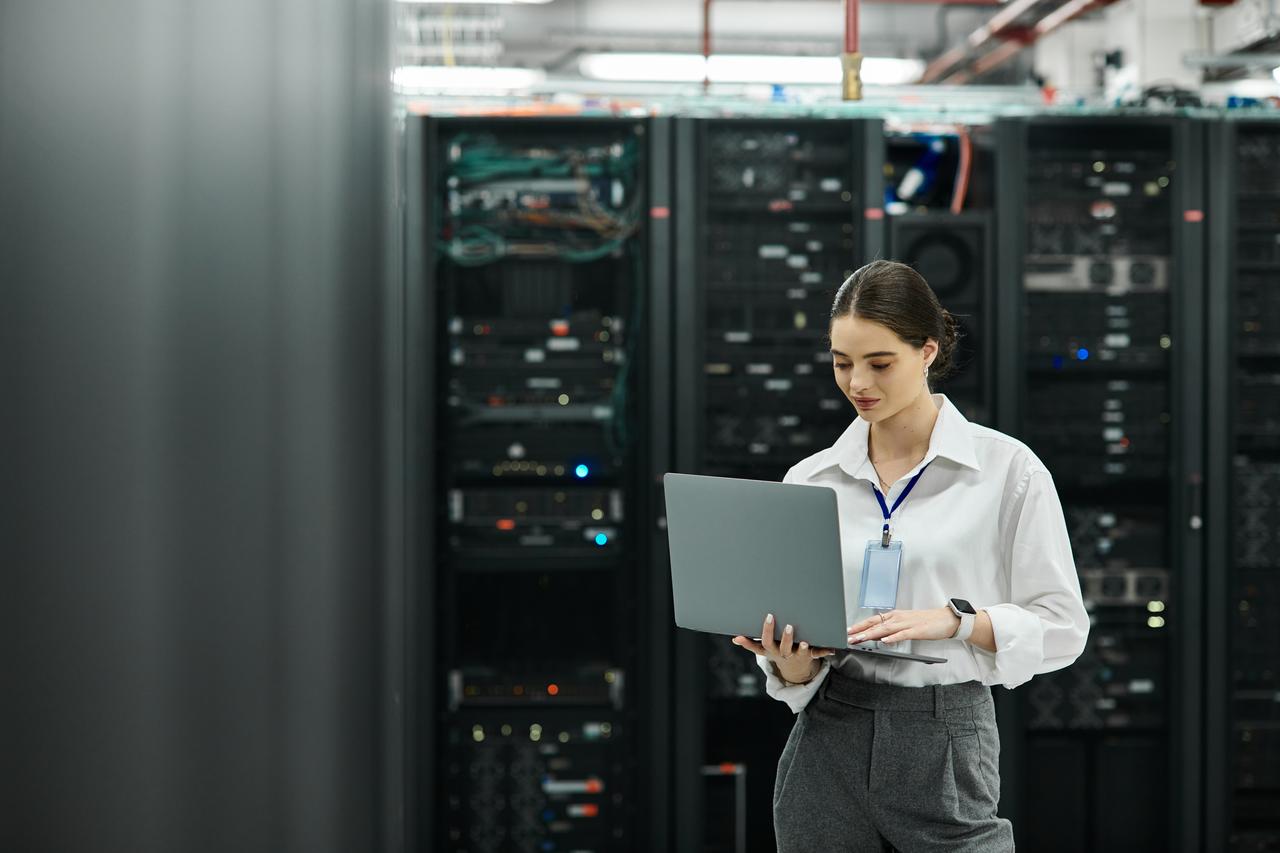 A technology professional works on a laptop in a data center surrounded by server racks. (Adobe Stock Photo)