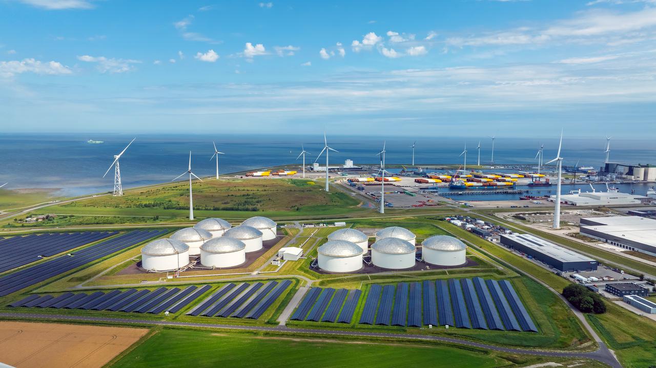 An aerial view shows wind turbines, solar panels and industrial storage tanks at a coastal energy facility. (Adobe Stock Photo)