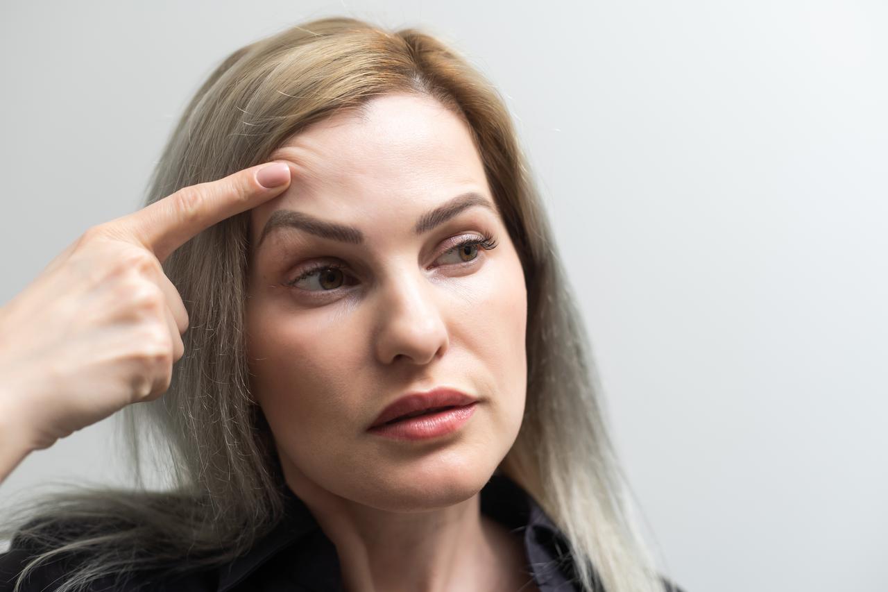 A woman points to her forehead, illustrating facial skin concerns and cosmetic treatments. (Adobe Stock Photo)