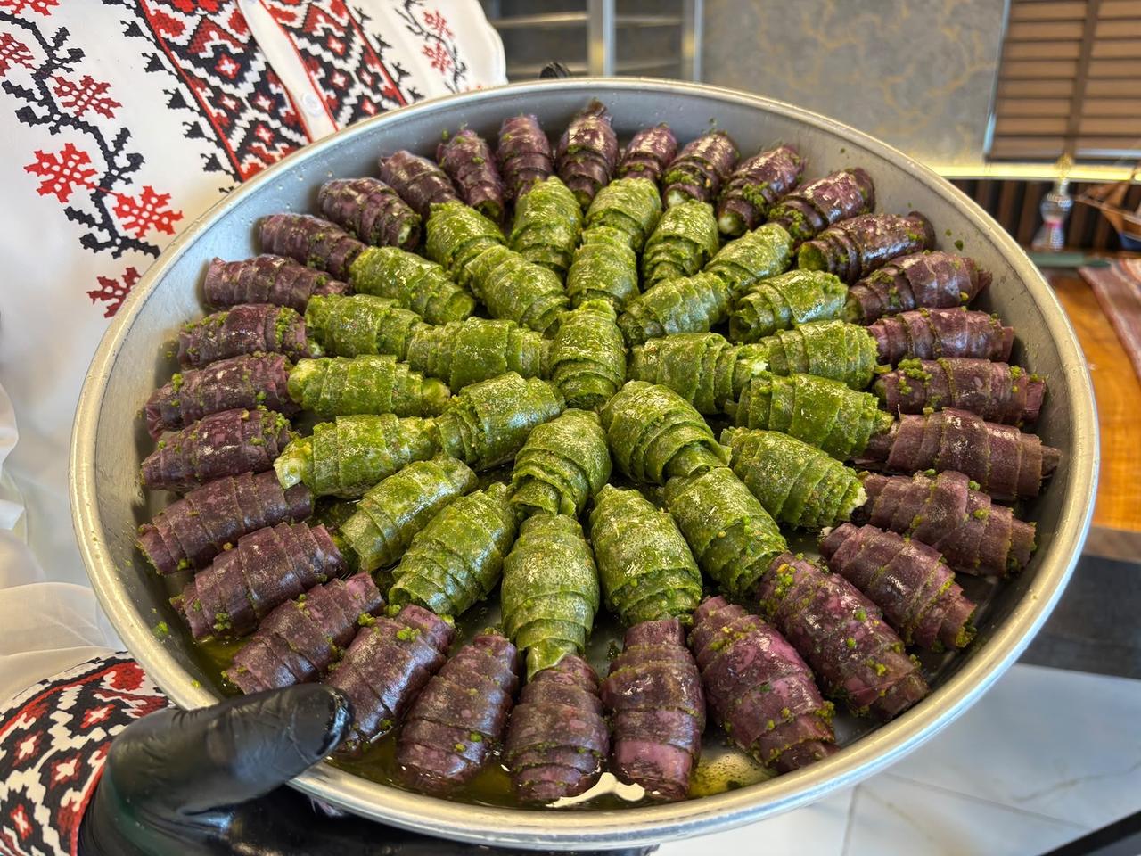 Green and purple croissant-shaped baklava pastries, filled with pistachios and coated in syrup, are arranged on a tray in Gaziantep, Türkiye, Oct. 28, 2026. (IHA Photo)
