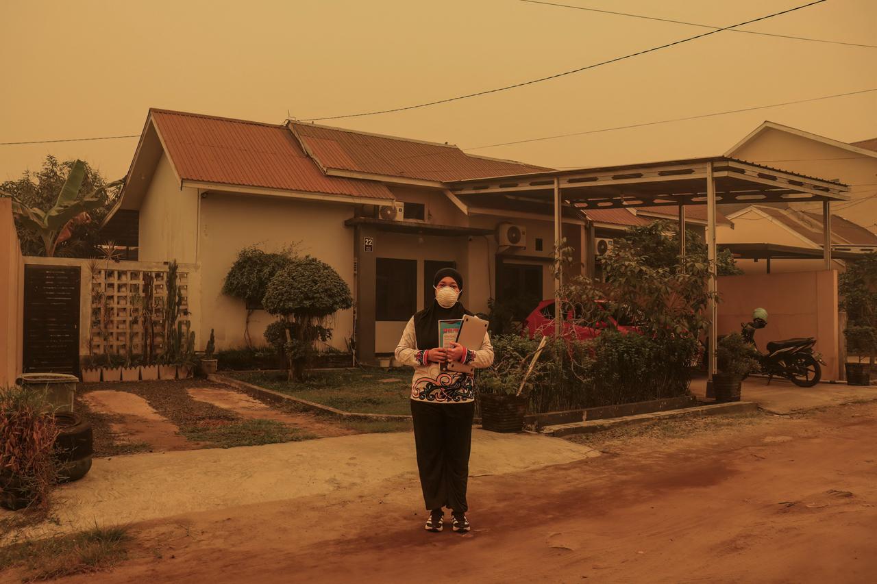 This picture taken on Oct. 23, 2026 shows Yuni Kartika posing in front of her residence amid thick haze resulting from forest and land fires in Palangkaraya, Central Kalimantan province. (AFP Photo)