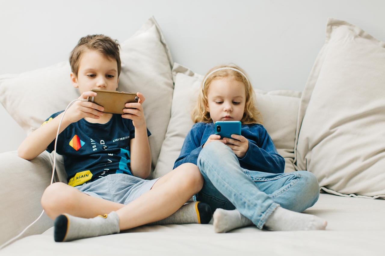 2 children sit on gadgets and play on phones. (Adobe Stock photo)