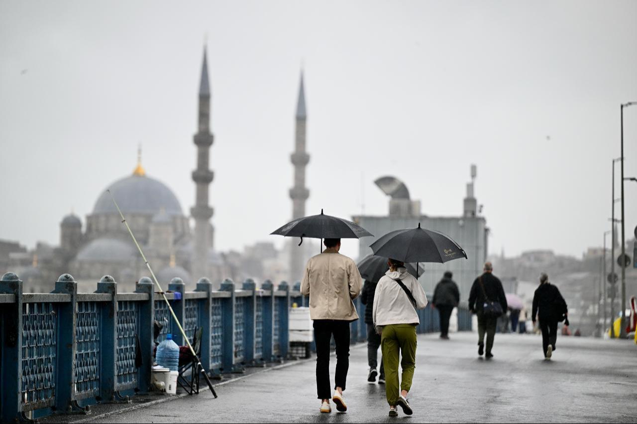 Pedestrians walk under umbrellas on Galata Bridge, with a mosque visible in the background, during rainy weather in Istanbul, Türkiye, Oct. 15, 2026. (AA Photo)