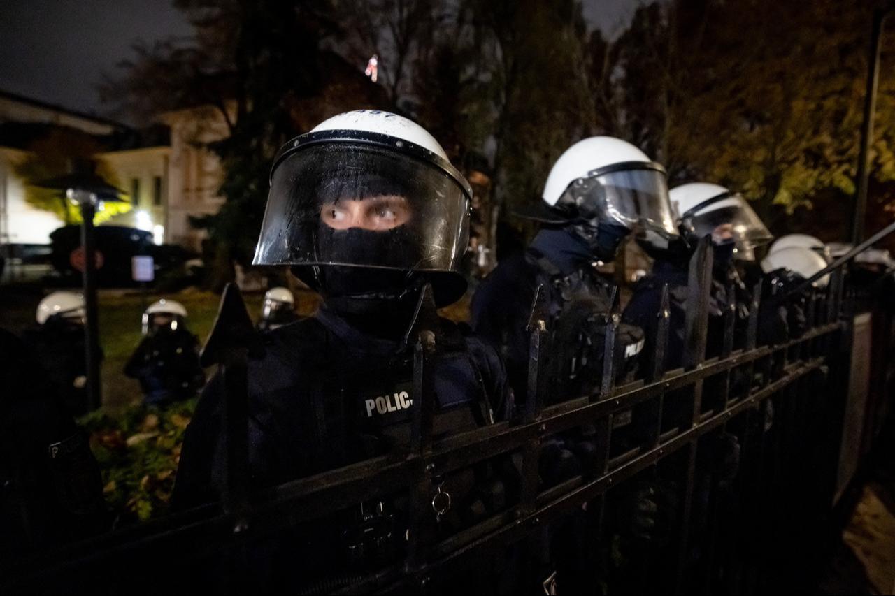 Police officers stand behind the fence as protesters gather outside the headquarters of Poland's Constitutional Court in Warsaw after police blocked access to the court building on 30 Oct., 2026 (AFP Photo)
