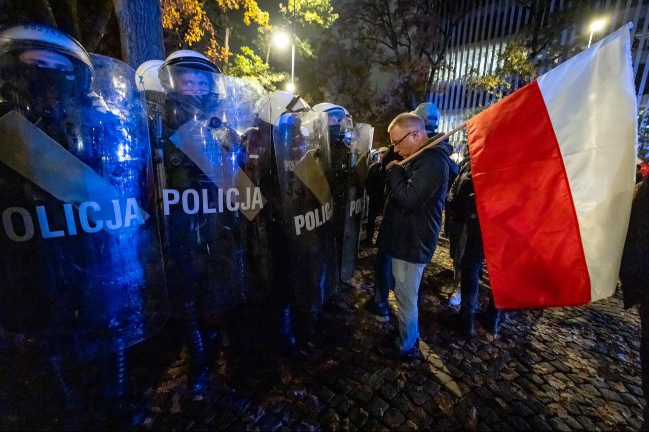 A man holding a Polish national flag stands ian front of police officers in riot gear as protesters gather outside the headquarters of Poland's Constitutional Court in Warsaw after police blocked access to the building on Oct. 30, 2026. (AFP Photo)