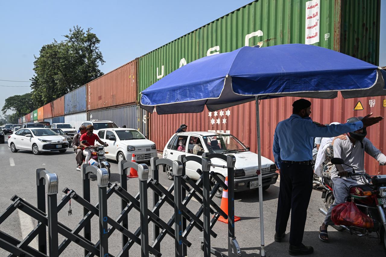 Commuters drive past shipping containers blocking a road towards the Red Zone area in Islamabad on October 2, 2026 ahead of a protest by the Pakistan Tehreek-e-Insaf (PTI) party to demand the release of jailed former prime minister Imran Khan. (AFP Photo)