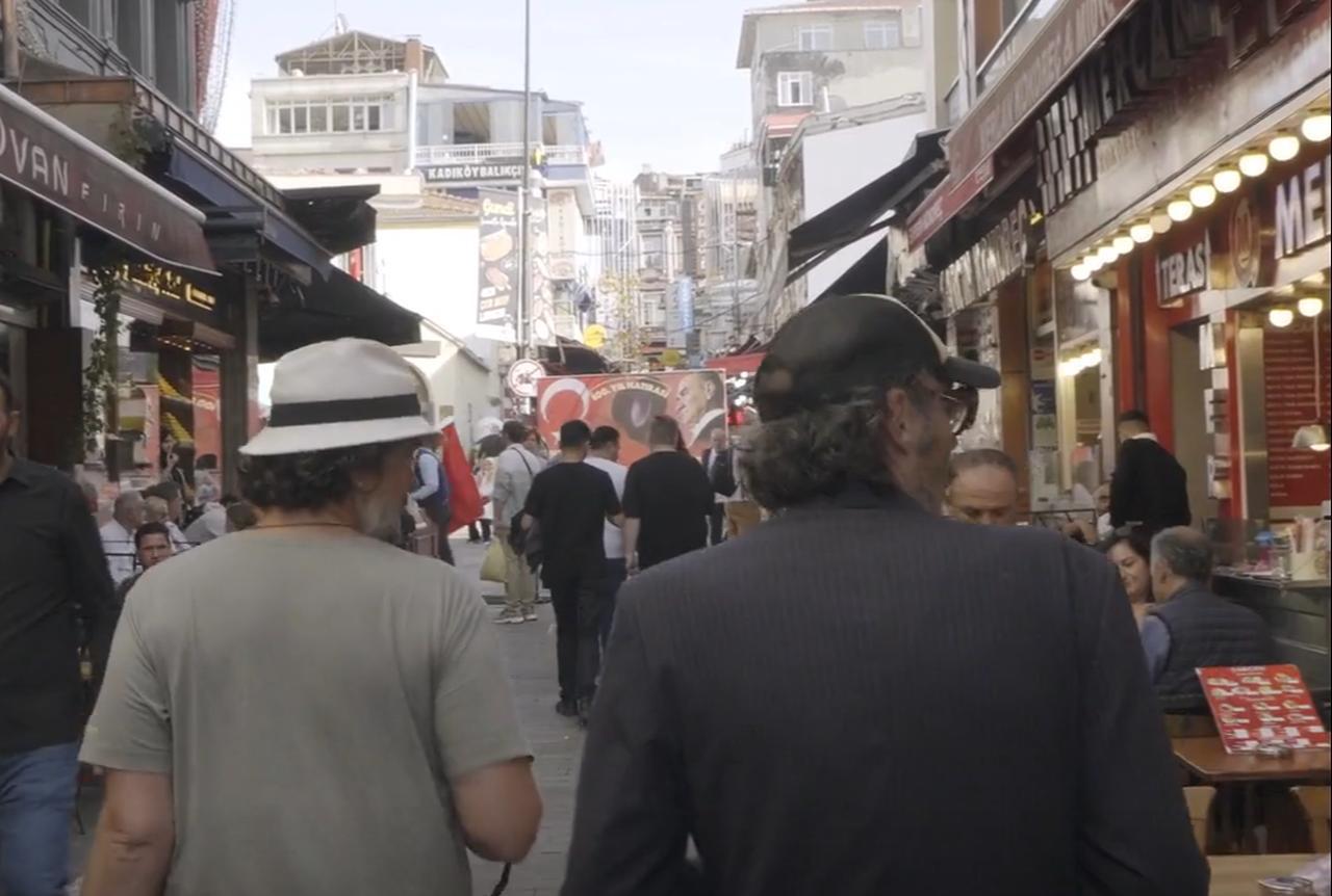 Mathias Mlekuz and Philippe Rebbot walk through a crowded Istanbul street lined with shops and restaurants in "A Bicyclette!." (Image via M.E.S. Productions, F Comme Film)