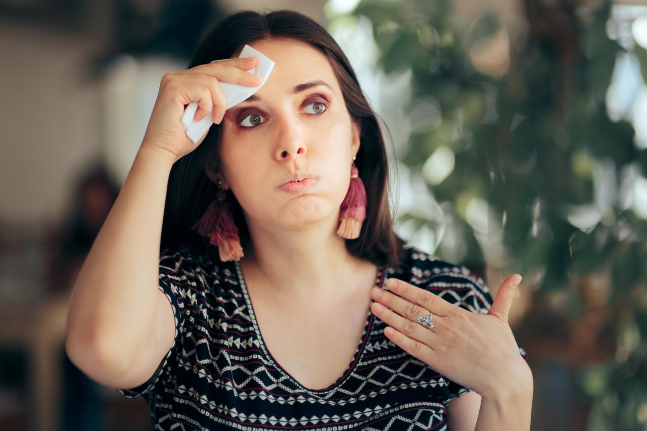 A woman wipes sweat from her forehead, illustrating discomfort during hot weather. (Adobe Stock Photo)
