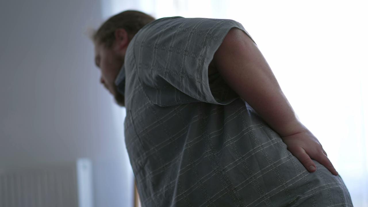 A person bends forward while holding their lower back, illustrating back pain and discomfort. (Adobe Stock Photo)