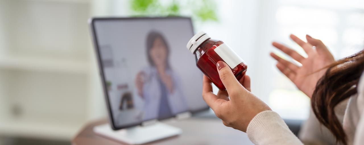 A patient holds a medicine bottle during an online consultation with a health professional. (Adobe Stock Photo)