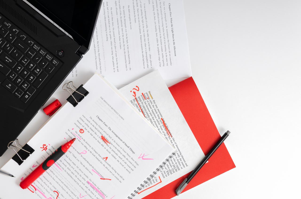 Papers with highlighted text, notes and a laptop are arranged on a desk in an illustrative image representing writing and editing work. (Adobe Stock Photo)
