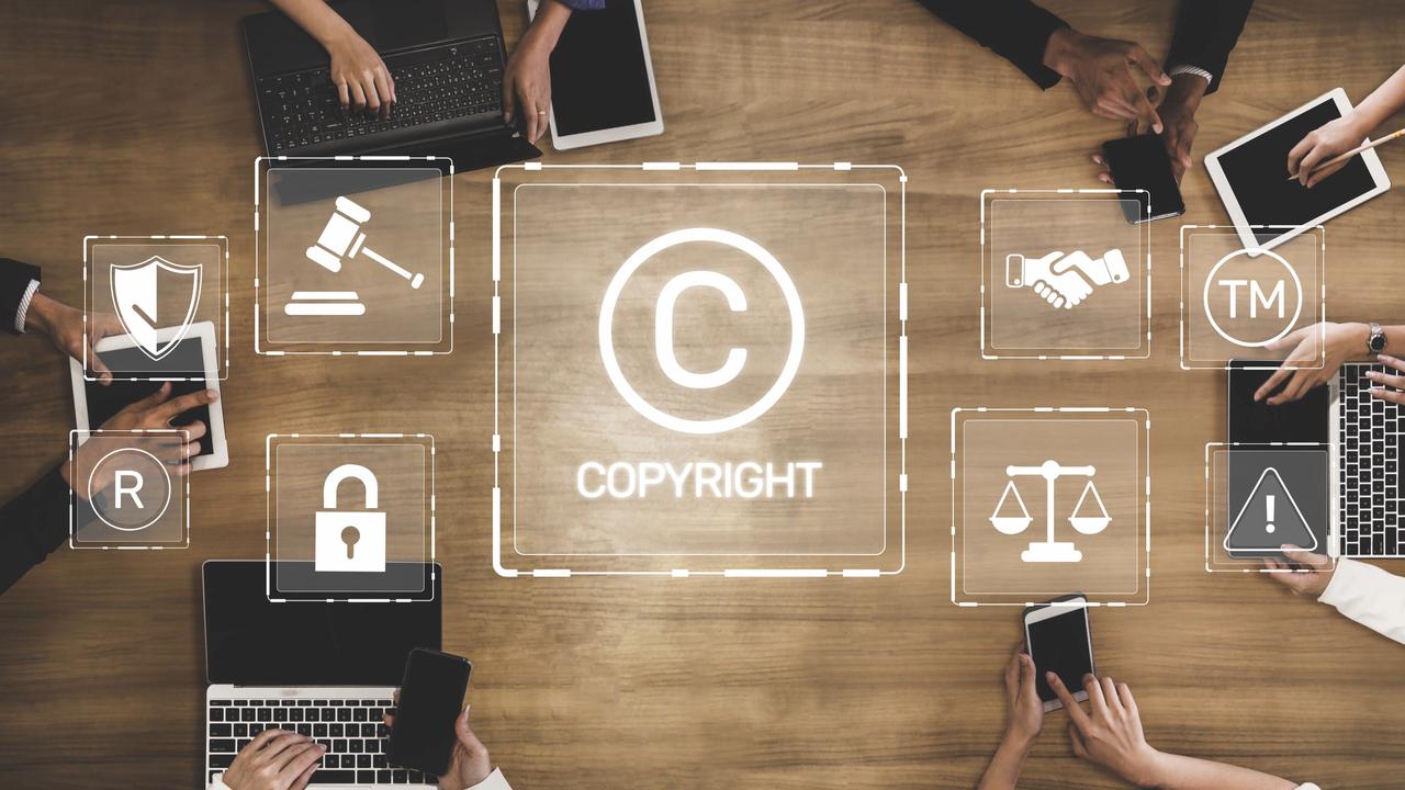 Copyright and intellectual property symbols appear over a workspace with digital devices, illustrating copyright protection and legal rights. (Adobe Stock Photo)