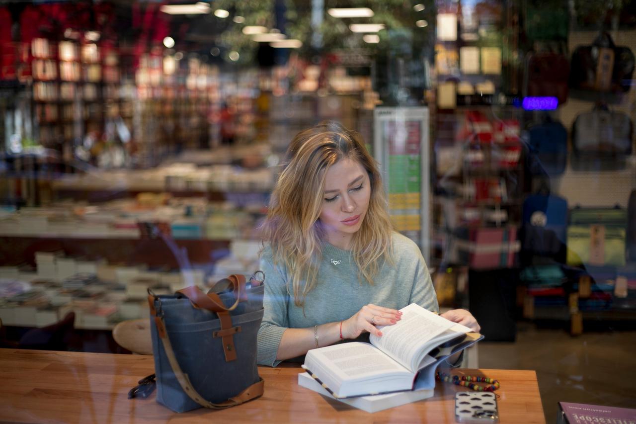 A woman reads a book inside a bookstore, illustrating reading and the publishing industry. (Adobe Stock Photo)
