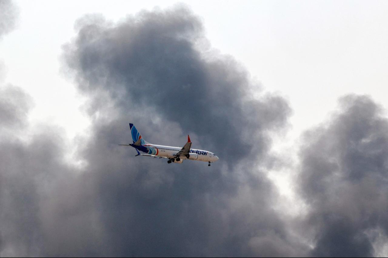 A Flydubai Boeing 737 Max aircraft prepares for landing as a smoke plume rises from an ongoing fire near Dubai International Airport in Dubai on March 16, 2026. (AFP Photo)
