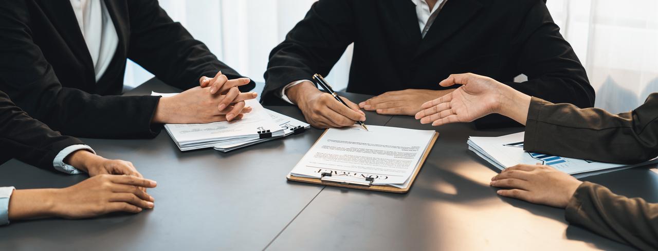 Business representatives discuss and review a contract during a meeting, illustrating negotiations and agreement talks. (Adobe Stock Photo)