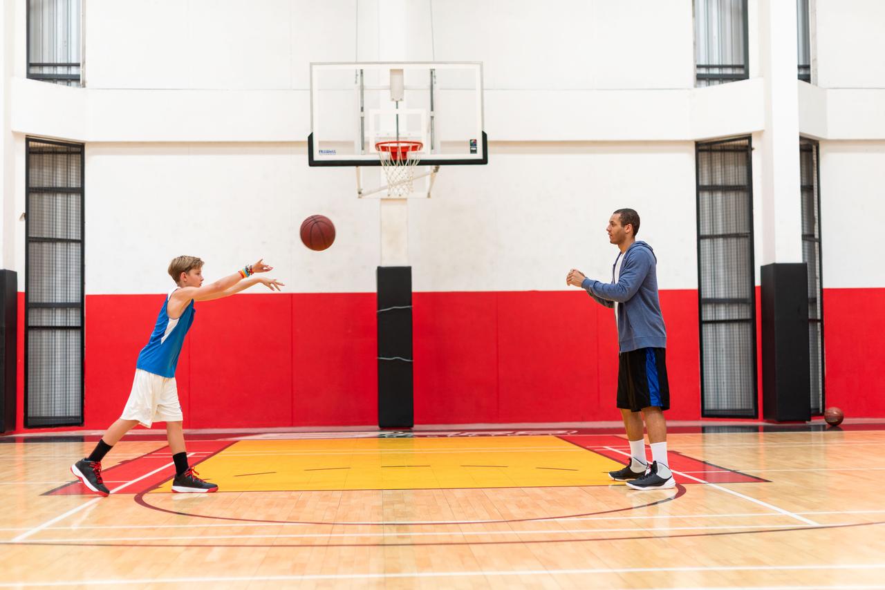 A young basketball player practices passing with an adult coach inside an indoor gym, illustrating youth basketball training and development. (Adobe Stock Photo)
