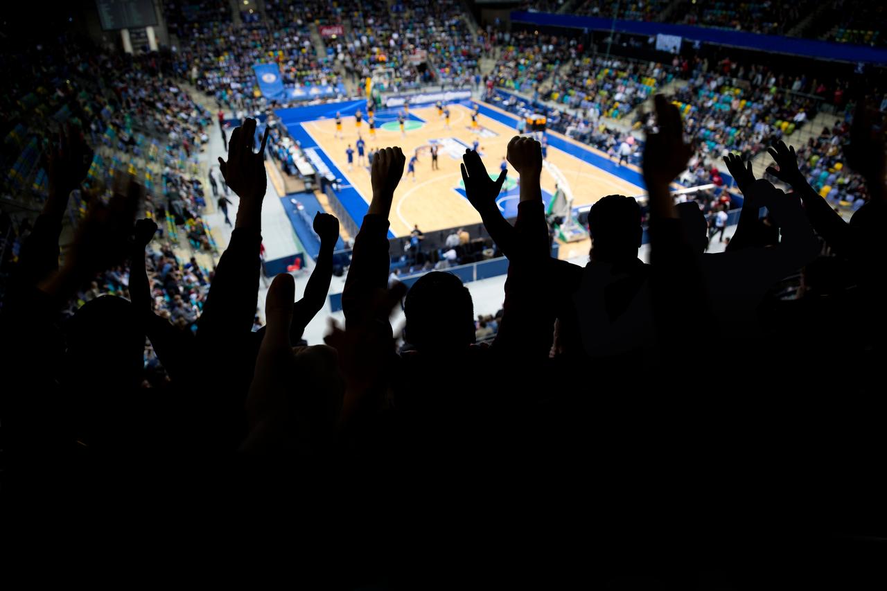 Fans cheer from the stands during a basketball game inside a packed indoor arena. (Adobe Stock Photo)