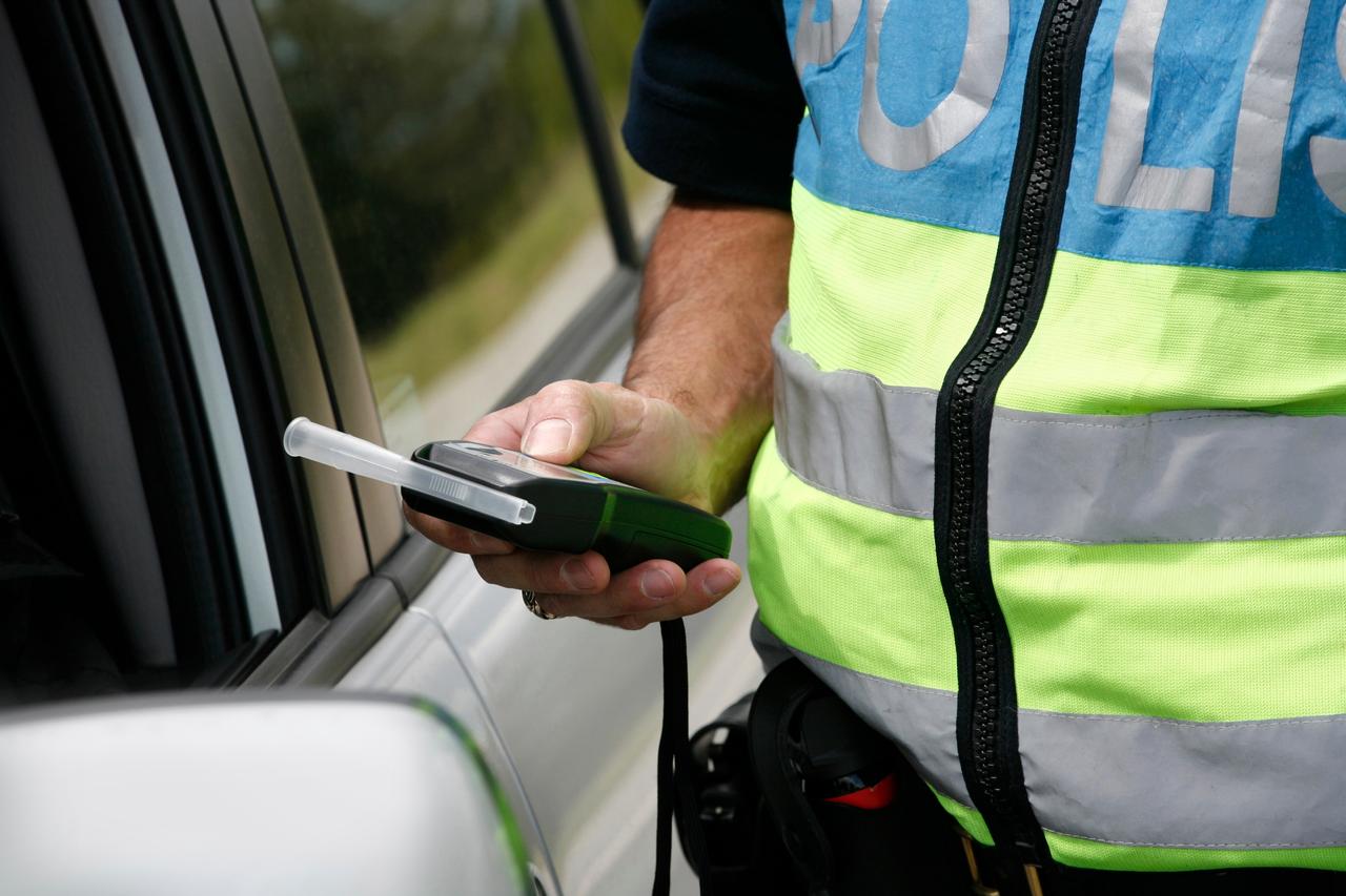 Traffic police officer conducting a roadside alcohol test with a breathalyzer device. (Adobe Stock Photo)