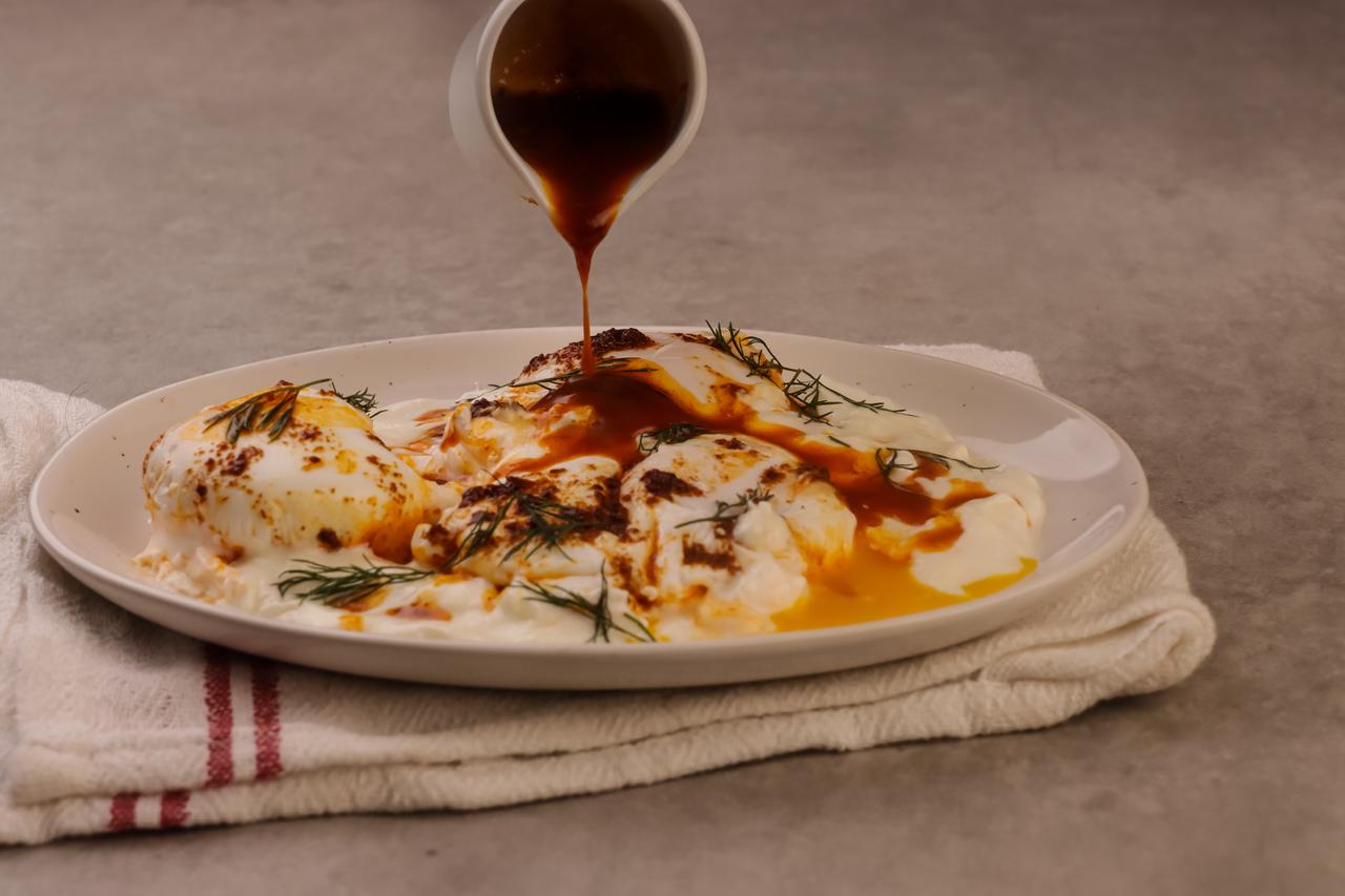 Poached eggs served over creamy garlic yogurt and topped with warm red pepper butter sauce, a traditional cilbir dish from Türkiye. (Adobe Stock Photo)
