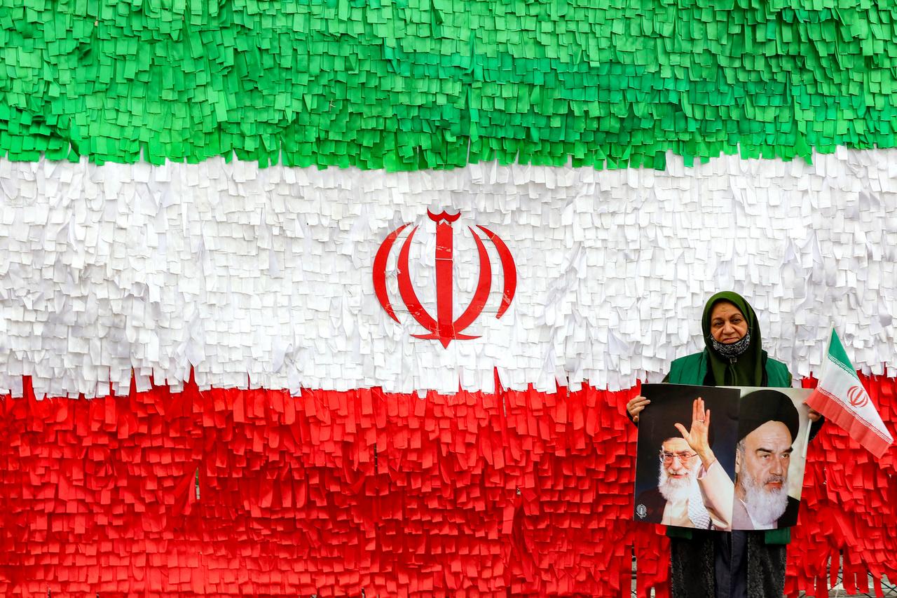 A woman poses with photos of Iran's late and current supreme leaders as she stands before an installation depicting the Iranian flag during a rally in Tehran, Feb. 11, 2026. (AFP Photo)