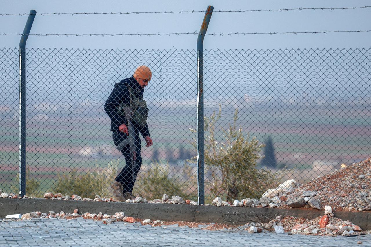 A guard patrols outside a barbed-wire fence outside the Akbaran camp near Akhtarin, in the north of Aleppo province, on February 17, 2026. (AFP Photo)