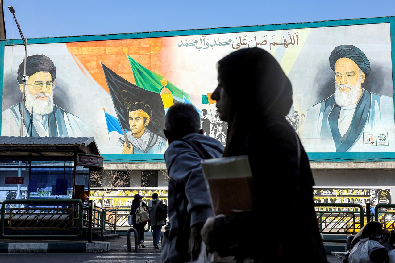 A woman walks near a banner depicting Iran's late and current supreme leaders (R to L) Ayatollah Ruhollah Khomeini and Ayatollah Ali Khamenei along a main street in Tehran, February 21, 2026. (AFP Photo)