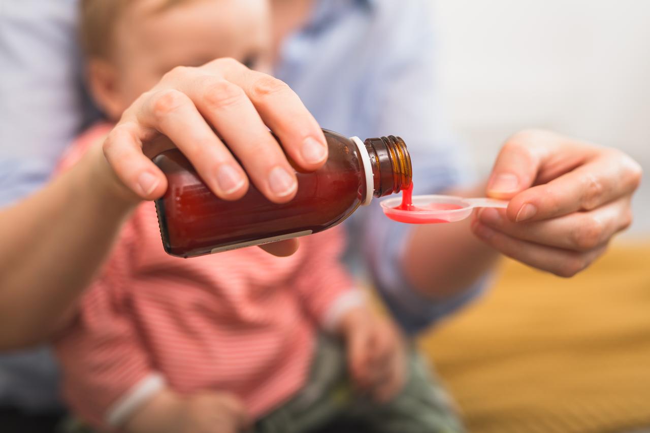A caregiver pours liquid acetaminophen into a dosing spoon to administer medicine to a child. (Adobe Stock Photo)