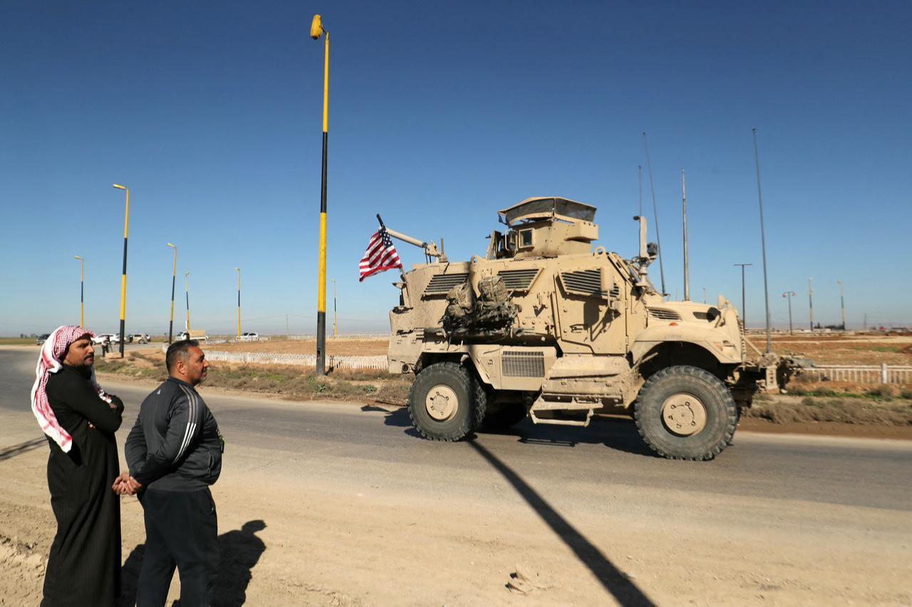 Men watch as a US military mine-resistant ambush protected (MRAP) armoured fighting vehicle moves in a convoy along a highway outside Qamishli in Syria's northeastern Hasakah province, Feb. 23, 2026. (AFP Photo)