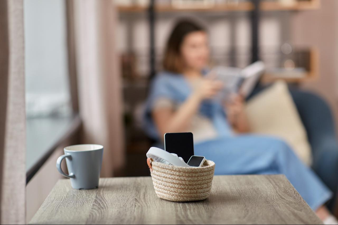 Close up of gadgets in basket on table and woman reading book at home (Adobe Stock Photo)
