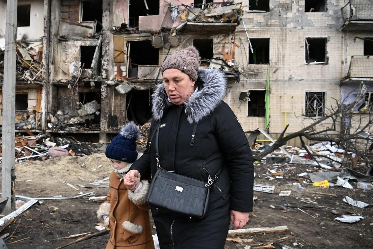 A woman with a child walks in front of a damaged residential building at Koshytsa Street, a suburb of the Ukrainian capital Kyiv, February, 2022. (AFP Photo)