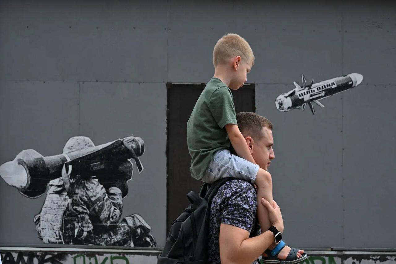 A man carries his son as they walk past graffiti on a wall depicting a Ukrainian serviceman making a shot with a U.S.-made Javelin portable anti-tank missile system in Kyiv, Ukraine, July 29, 2022. (AFP Photo)