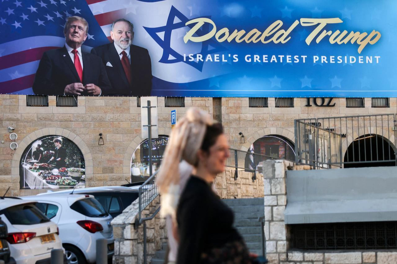 People walk next to a sign with portraits of US President Donald Trump (L) and US Ambassador to Israel Mike Huckabee in central Jerusalem on May 7, 2025. (AFP Photo)