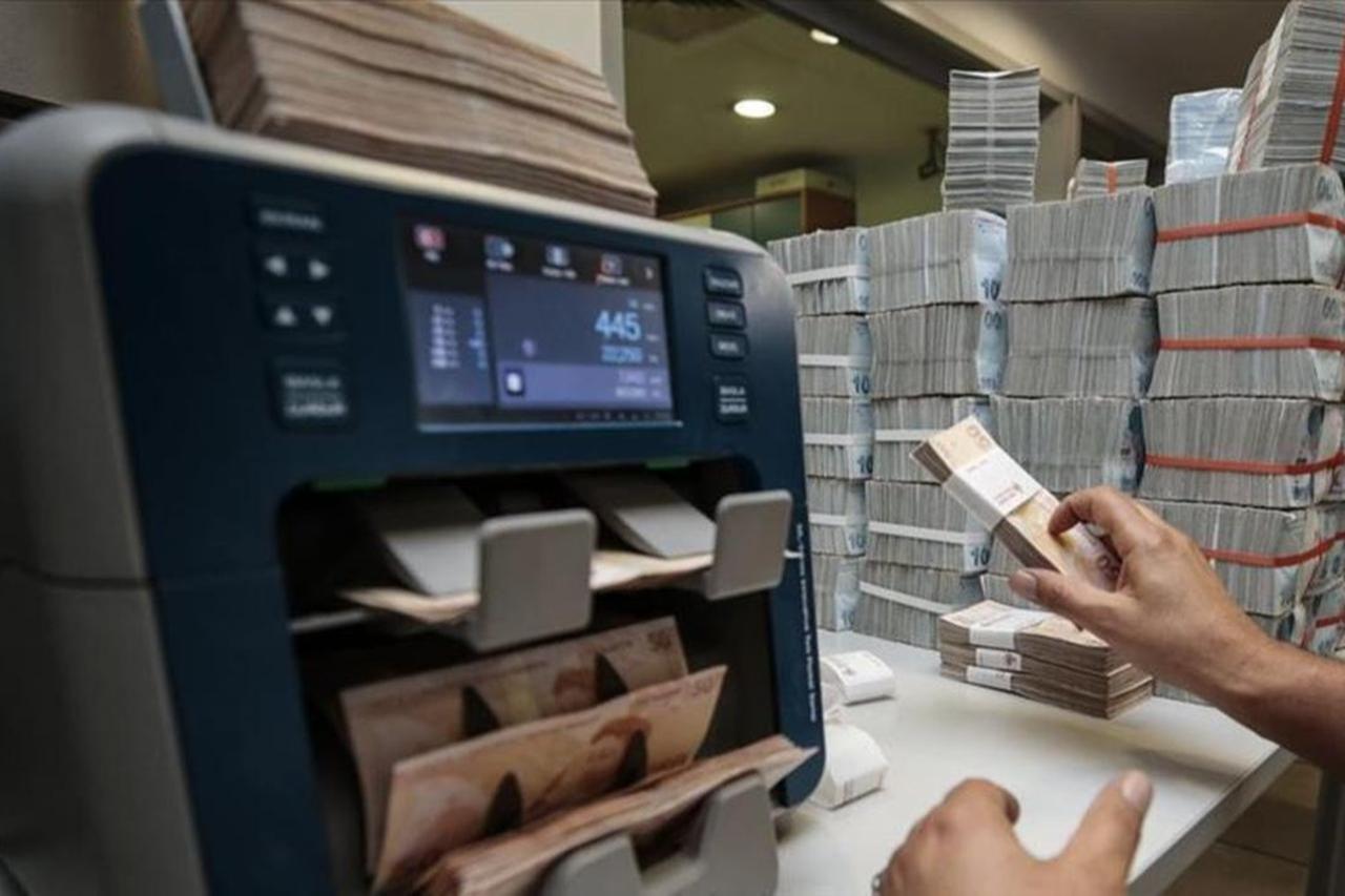 A bank employee counts Turkish lira banknotes with a currency counter in Türkiye. (AA Photo)