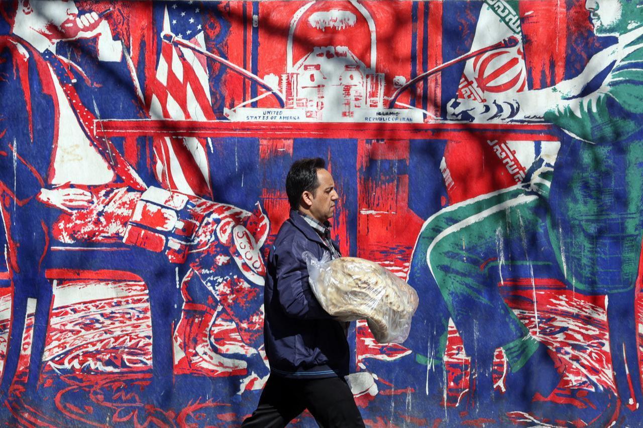 An Iranian man carrying breads walk past an anti-US mural featuring Iran-US talks, next to the former US embassy in Tehran on Feb. 26, 2026. (AFP Photo)