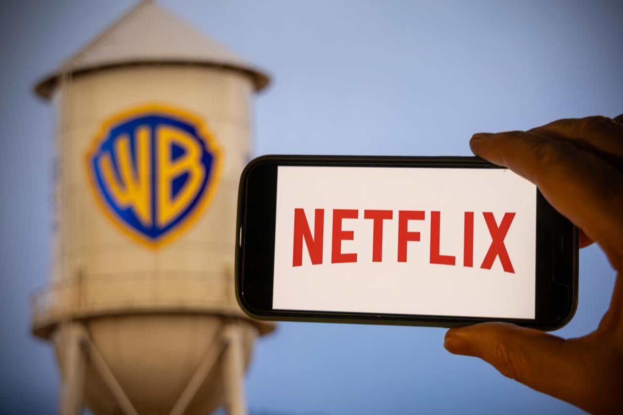 A phone displaying the Netflix logo is held in front of Warner Bros.’ iconic Hollywood water tower in California, U.S. (Adobe Stock Photo)