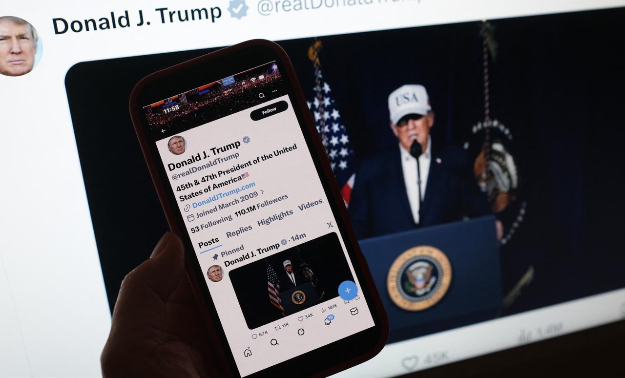 This illustration image shows a person looking at a smartphone displaying US President Donald Trump making a statement regarding combat operations on Iran, alongside a computer screen featuring the same message posted on X on February 28, 2026. (AFP Photo)
