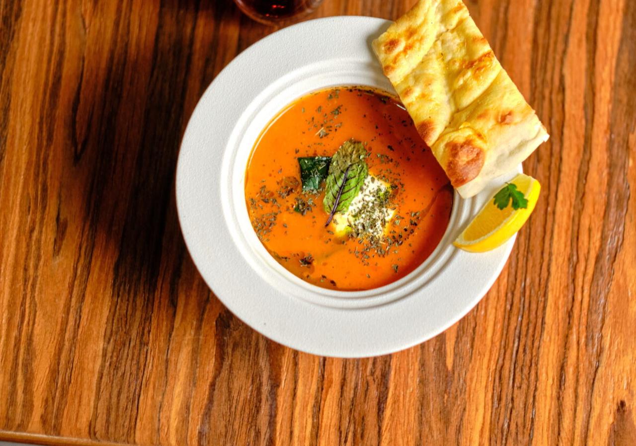 A bowl of tarhana soup, a Turkish fermented soup with a creamy texture, served with pita bread, tea, and lemon on a wooden table. (Adobe Stock Photo)
