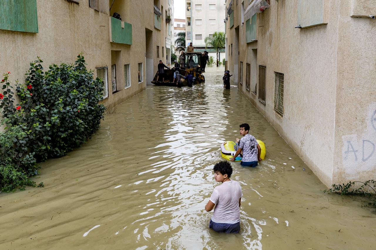 A boy pushes another riding in an inflatable floater along an inundated street with others sitting atop a bulldozer in Morocco's northwestern city of Ksar el-Kebir on January 29, 2026.(AFP Photo)