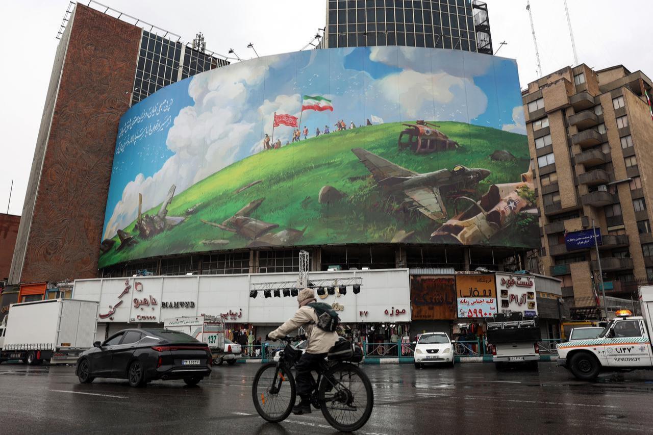 A cyclist rides past an anti-US billboard displayed on a building in Tehran's Valiasr Square, February 4, 2026. (AFP Photo)
