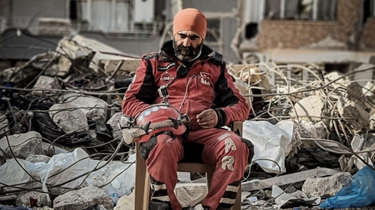 A SAR rescue worker in a red uniform sits on a chair in the middle of debris, Hatay, Türkiye, February, 2023. (Courtesy of SAR)